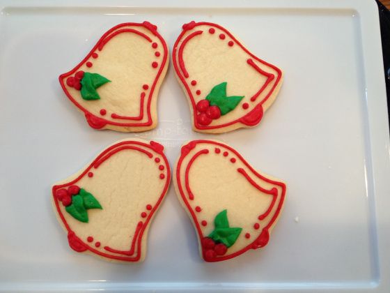 Cheerful Holiday Cookies: Festive Bell Shapes Adorned with Intricate Red Icing and Green Leaf Details.