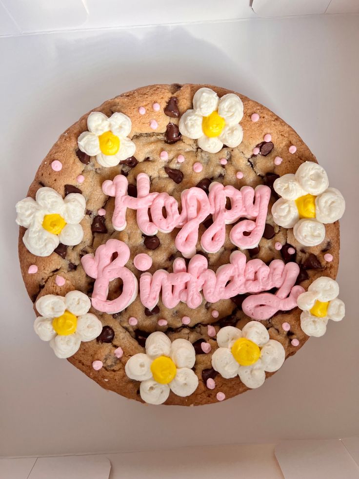 Cheerful Birthday Cookie Cake: Golden Base, Chocolate Chips, Whipped Cream Flowers, and Soft Pink Icing.