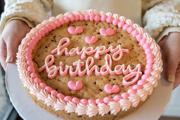 Festive Birthday Cookie Cake with Pastel Pink Frosting and Heart Patterns.