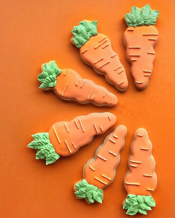 Whimsical Carrot-Shaped Cookies Adorned with Intricate Icing on a Vibrant Orange Background.