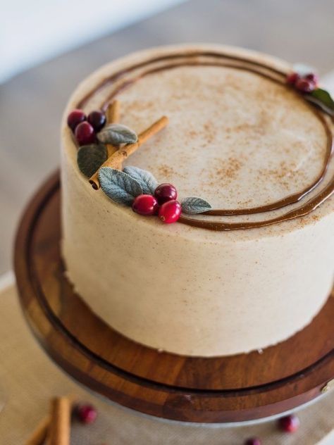 Festive Cake Design with Creamy Beige Frosting, Vibrant Cranberries, Green Leaves, and Cinnamon Sticks.