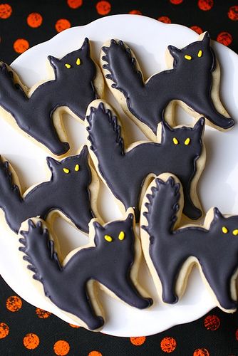 Adorable Halloween-themed cat-shaped cookies with glossy black icing and yellow accents.