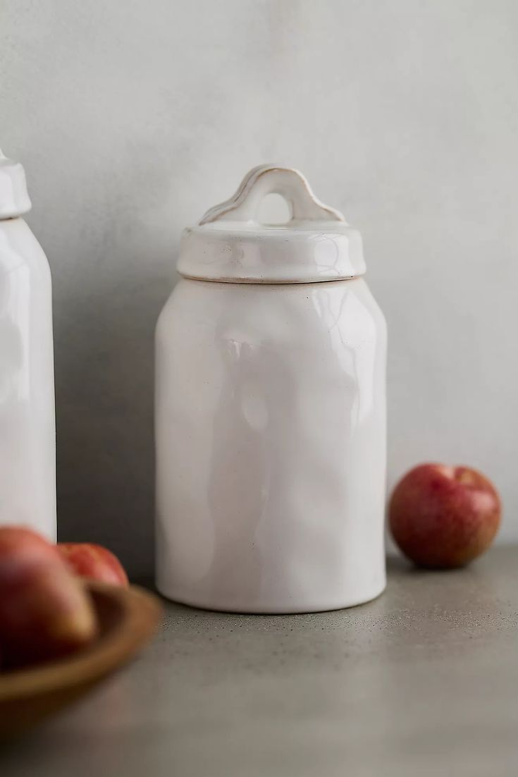 Elegant Ceramic Storage Jar with Glossy White Finish and Simple Lid, Perfect for Functional and Decorative Use, Accompanied by Fresh Red Apples.